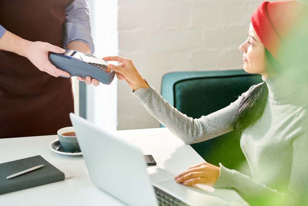 Side view portrait of modern young woman holding credit card and paying via NFC while working with laptop in cafe, copy space